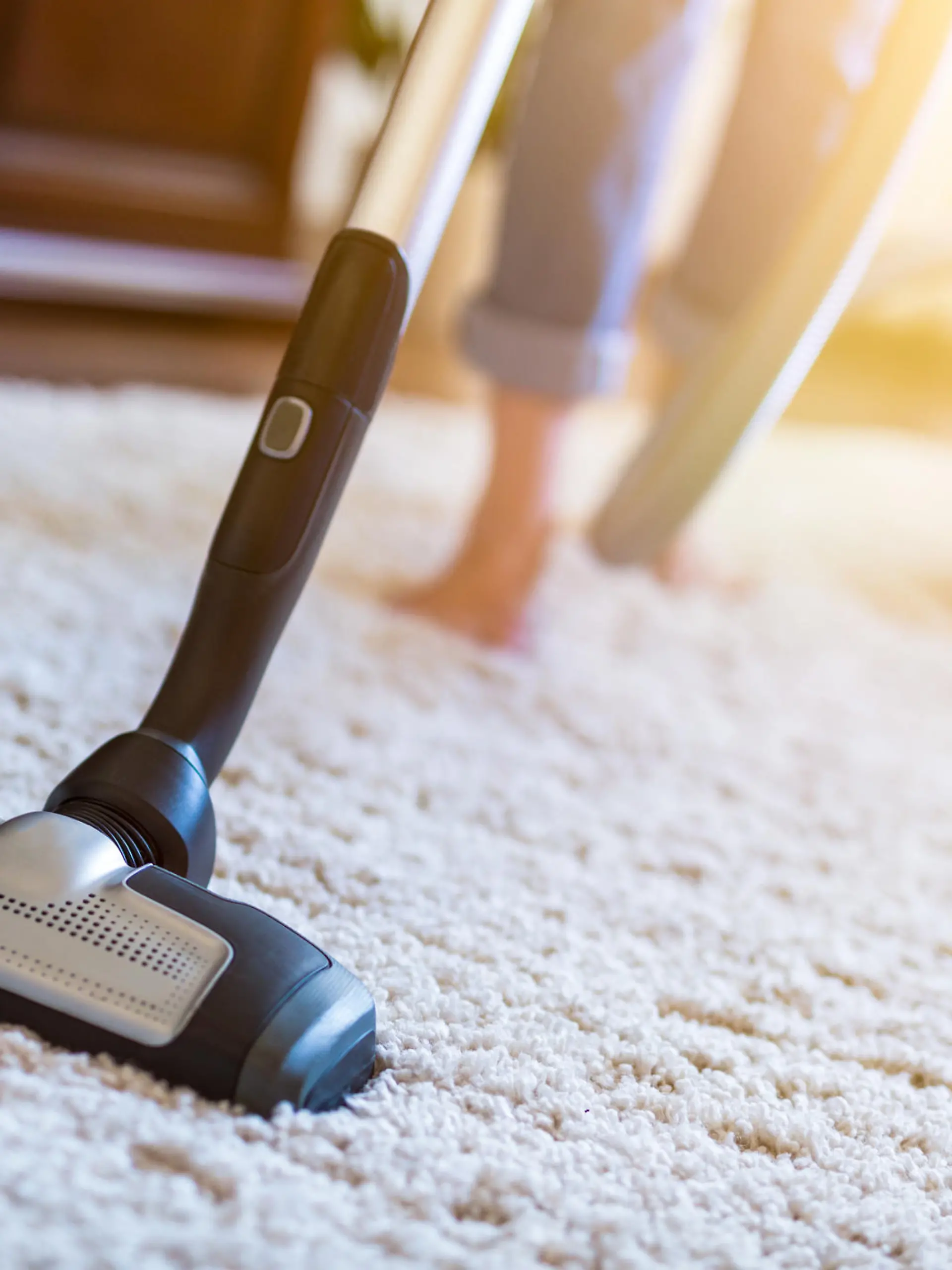 Young woman using a vacuum cleaner while cleaning carpet in the house.