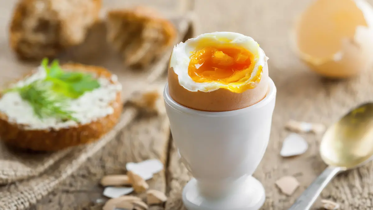 Ein perfekt gekochtes Frühstücksei steht im Fokus, im Hintergrund sieht man einen gedeckten Tisch, der zum Essen einlädt.