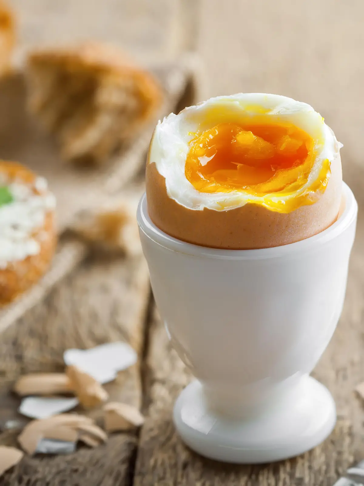 Ein perfekt gekochtes Frühstücksei steht im Fokus, im Hintergrund sieht man einen gedeckten Tisch, der zum Essen einlädt.