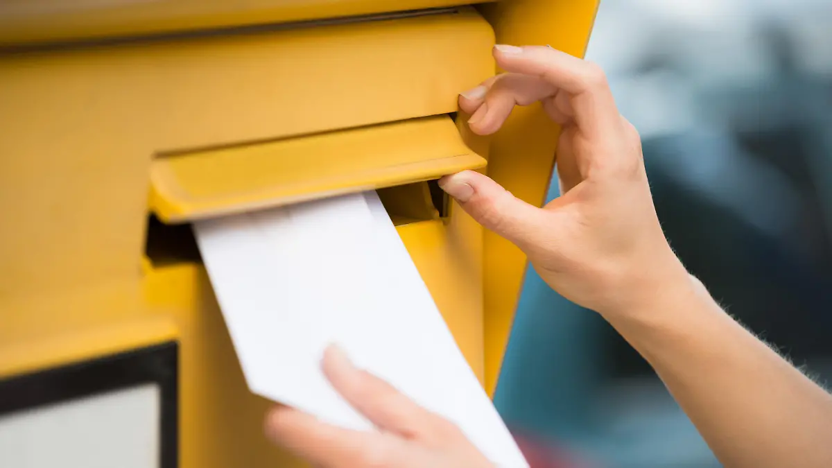 Man sieht wie jemand per Hand einen Brief in den Briefkasten steckt.
