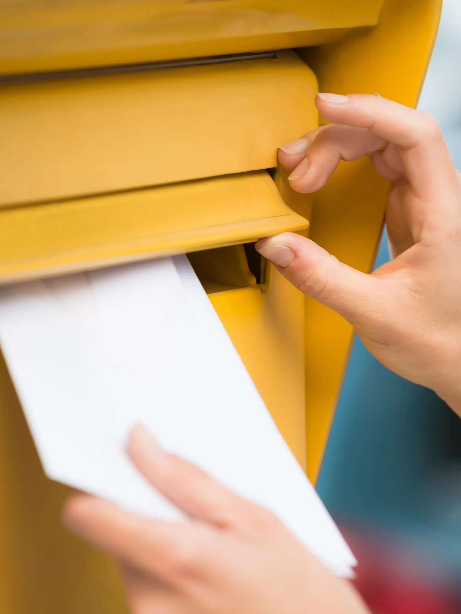 Man sieht wie jemand per Hand einen Brief in den Briefkasten steckt.
