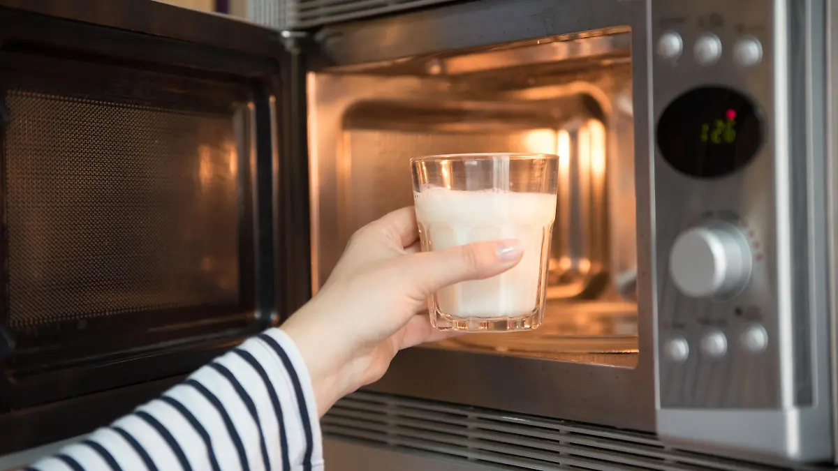 Frau stellt Glas mit Milch in die Mikrowelle