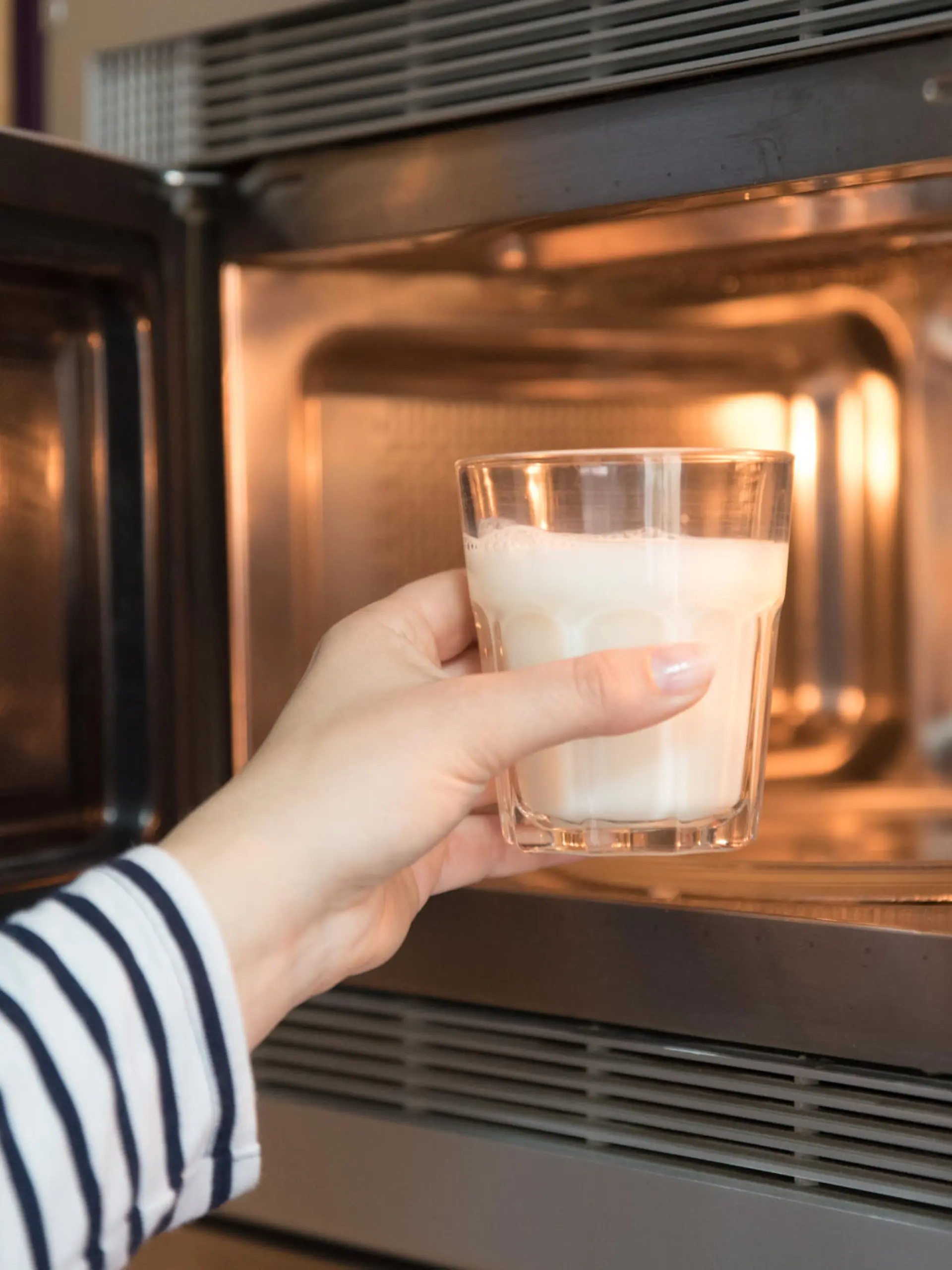 Frau stellt Glas mit Milch in die Mikrowelle