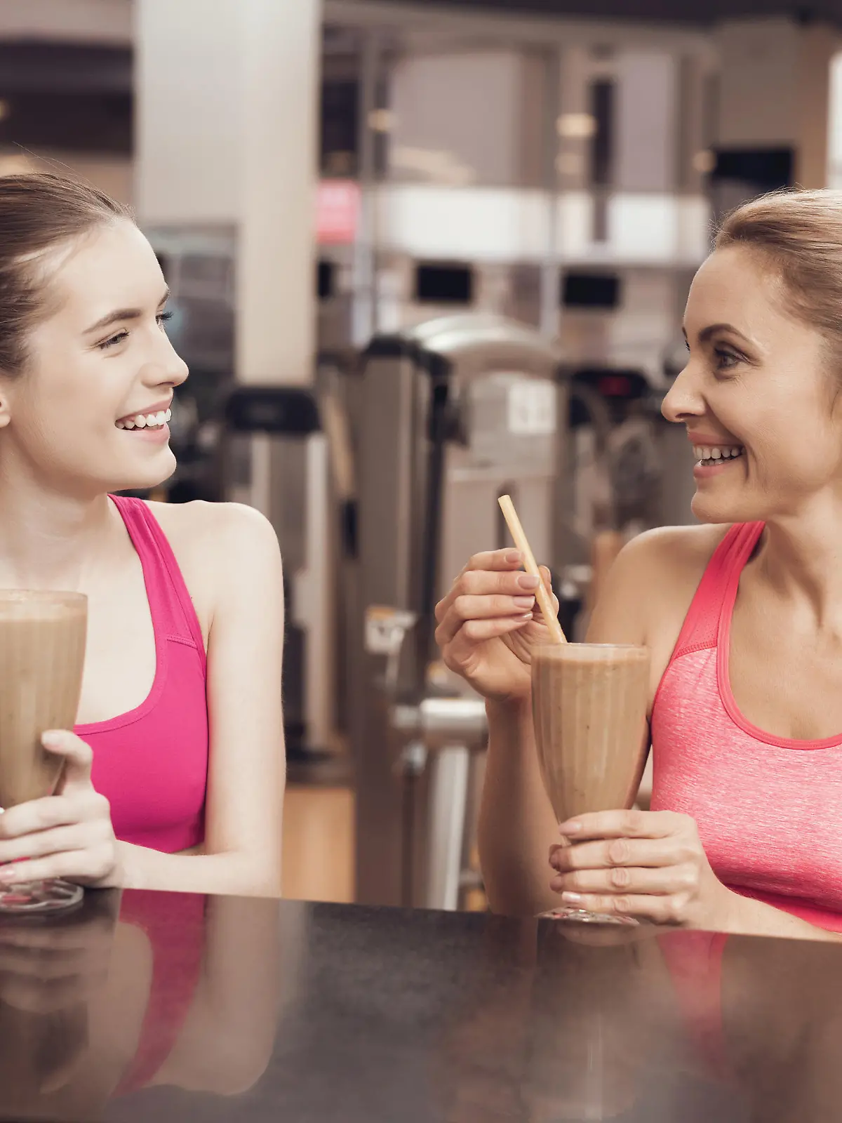 Eine Mutter und ihre Tochter trinken nach dem Training im Fitnessstudio einen Protein-Shake an der Bar.