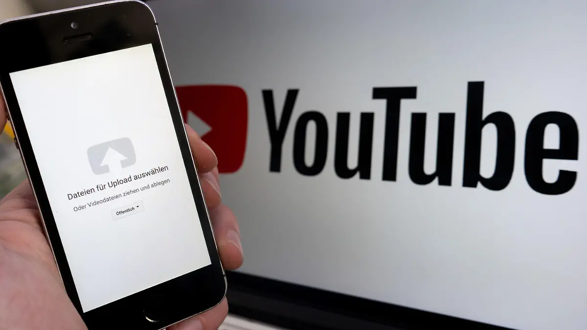 ILLUSTRATION - 14.02.2019, Niedersachsen, Hannover: - ARCHIV - Ein Upload-Fenster der Video-Plattform Youtube ist auf einem Smartphone vor einem YouTube-Logo auf einem Bildschirm zu sehen. (zu dpa: «Europaweiter Protest gegen neues Urheberrecht und Artikel 13») Foto: Raphael Knipping/dpa +++ dpa-Bildfunk +++