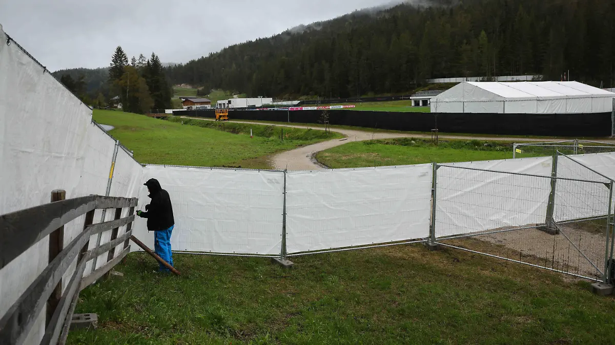 27.05.2021, Österreich, Seefeld: Ein Mitarbeiter befestigt weiße Planen an Sichtschutzzäunen unterhalb der Olympia-Sprungschanzen nahe der beiden Trainingsplätze, die die Deutsche Fußball-Nationalmannschaft während ihres Trainingslagers in Tirol vor der EM-Endrunde nutzen wird. Foto: Christian Charisius/dpa +++ dpa-Bildfunk +++