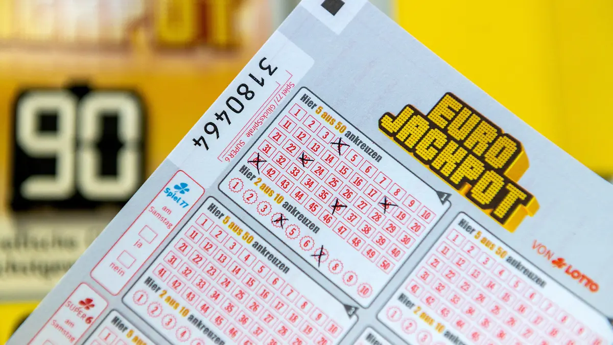 ILLUSTRATION - 06.02.2020, Baden-Württemberg, Freiburg: Ein Eurojackpot Los ist in einer Lotto-Annahmestelle vor einer Tafel zu sehen, auf der auf die Gewinnsumme von 90 Millionen im Eurojackpot hinwiesen wird. Zum zehnten Mal in seiner Geschichte hat der Eurojackpot seine maximale Gewinnhöhe erreicht. Am 07.02.2020 werden in Helsinki die Gewinnzahlen für diese europäische Lotterie gezogen, an der sich 18 Länder beteiligen. Foto: Patrick Seeger/dpa +++ dpa-Bildfunk +++