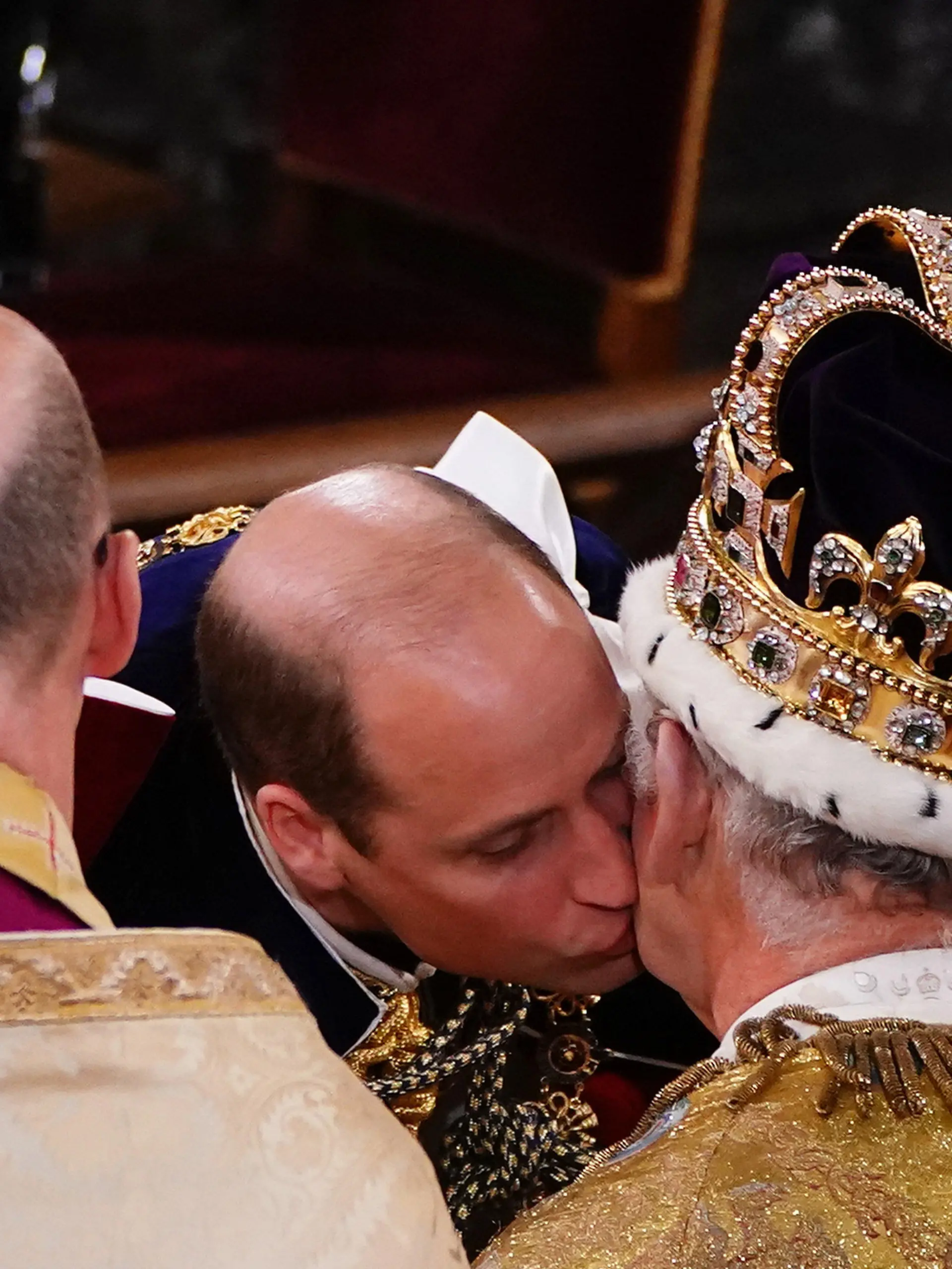 dpatopbilder - 06.05.2023, Großbritannien, London: William, Prinz von Wales, gibt seinem Vater König Charles III., der mit der Edwardskrone in einem Krönungsgewand auf dem Thron sitzt, während der Krönungszeremonie in der Westminster Abbey einen Kuss auf die Wange. Zur Krönung von König Charles III. sind zahlreiche Gäste gekommen. Foto: Yui Mok/PA Wire/dpa +++ dpa-Bildfunk +++