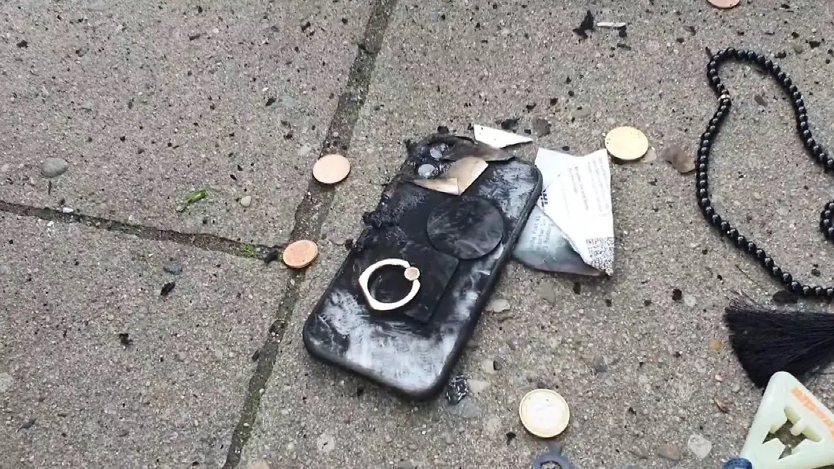 Ein verkohltes Handy liegt auf dem Gehweg.