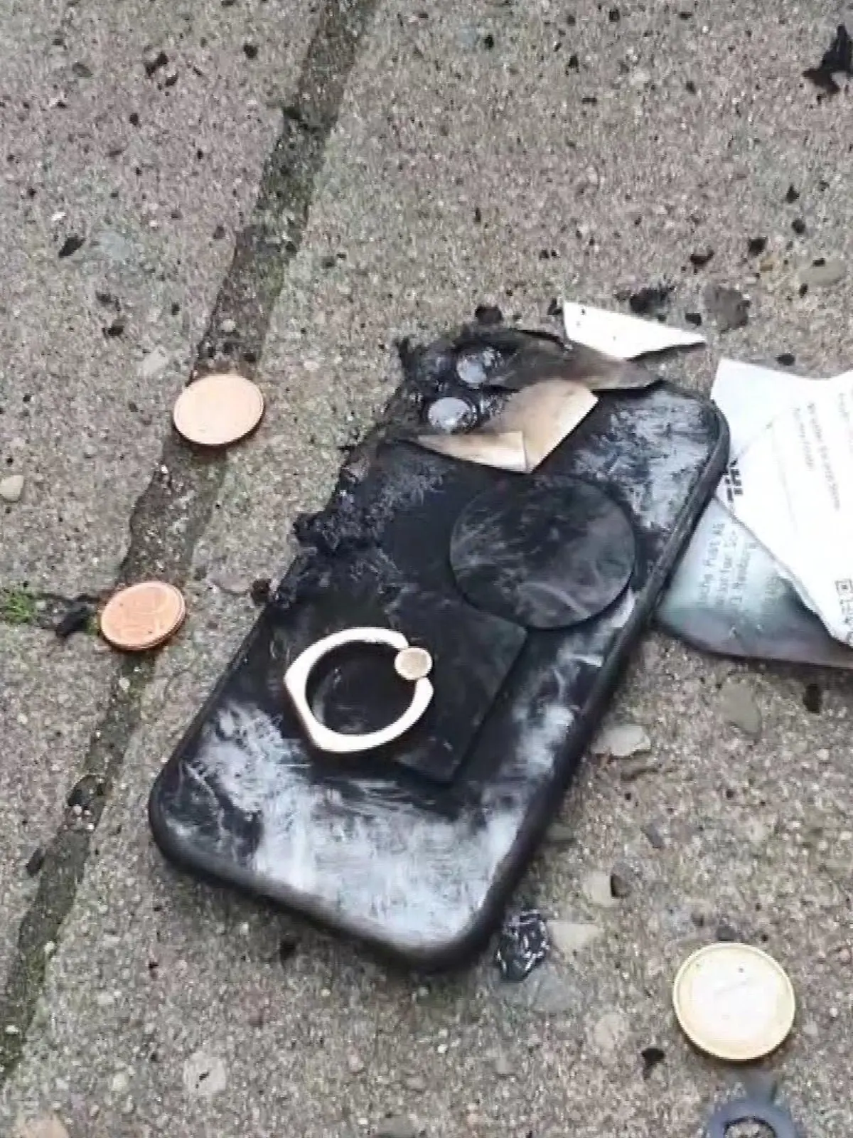 Ein verkohltes Handy liegt auf dem Gehweg.