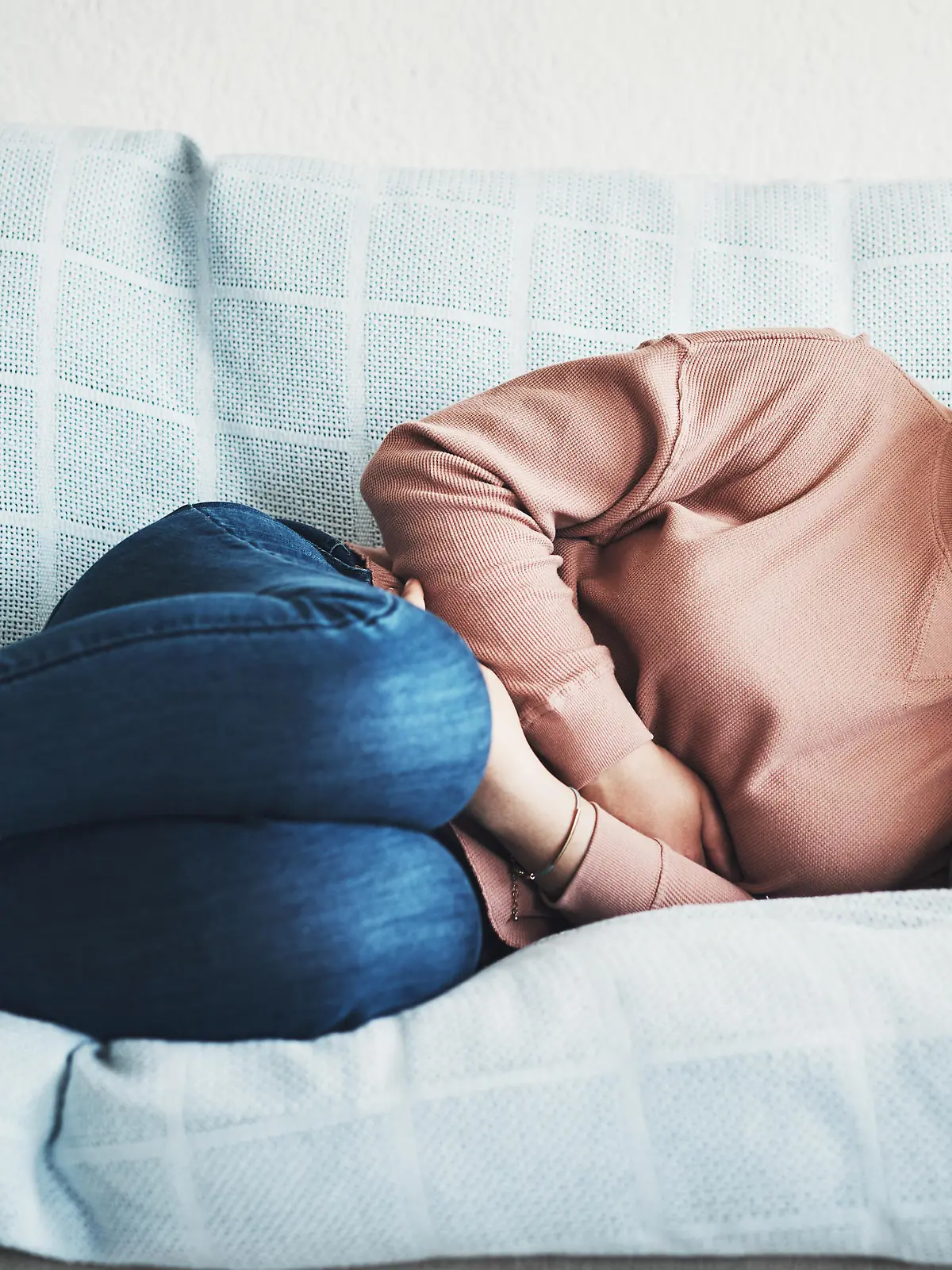 Frau liegt auf der Couch und hält sich vor Schmerzen den Bauch