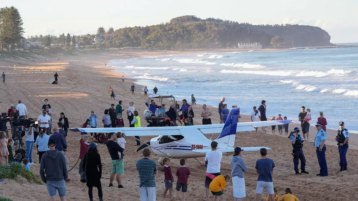 People stand near a light plane that made an emergency landing on a beach in Sydney Wednesday, May 26, 2021. The recreational plane landed safely on a Sydney beach with three people aboard including a baby on Wednesday after its single engine failed, officials said. (AP Photo/Mark Baker)
