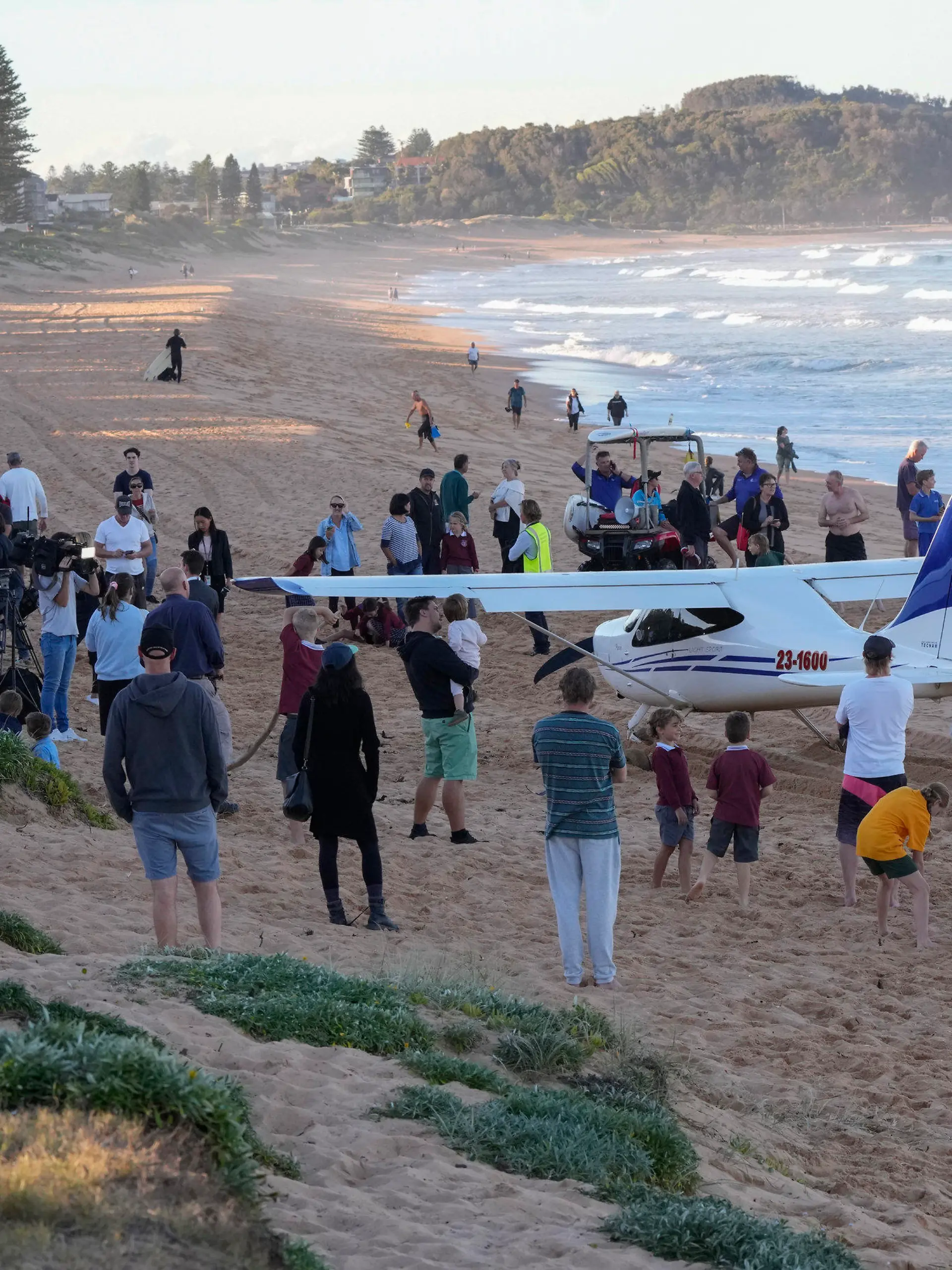 People stand near a light plane that made an emergency landing on a beach in Sydney Wednesday, May 26, 2021. The recreational plane landed safely on a Sydney beach with three people aboard including a baby on Wednesday after its single engine failed, officials said. (AP Photo/Mark Baker)