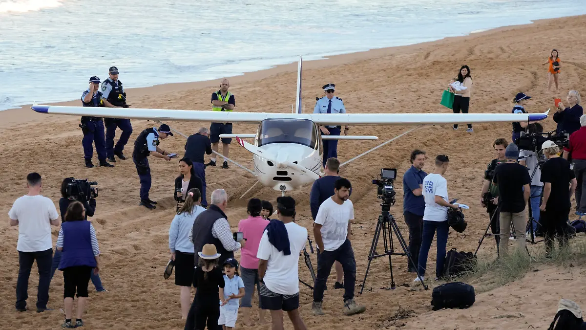 Spectators stand near a light plane that made an emergency landing on a beach in Sydney Wednesday, May 26, 2021. The recreational plane landed safely on a Sydney beach with three people aboard including a baby on Wednesday after its single engine failed, officials said. (AP Photo/Mark Baker)