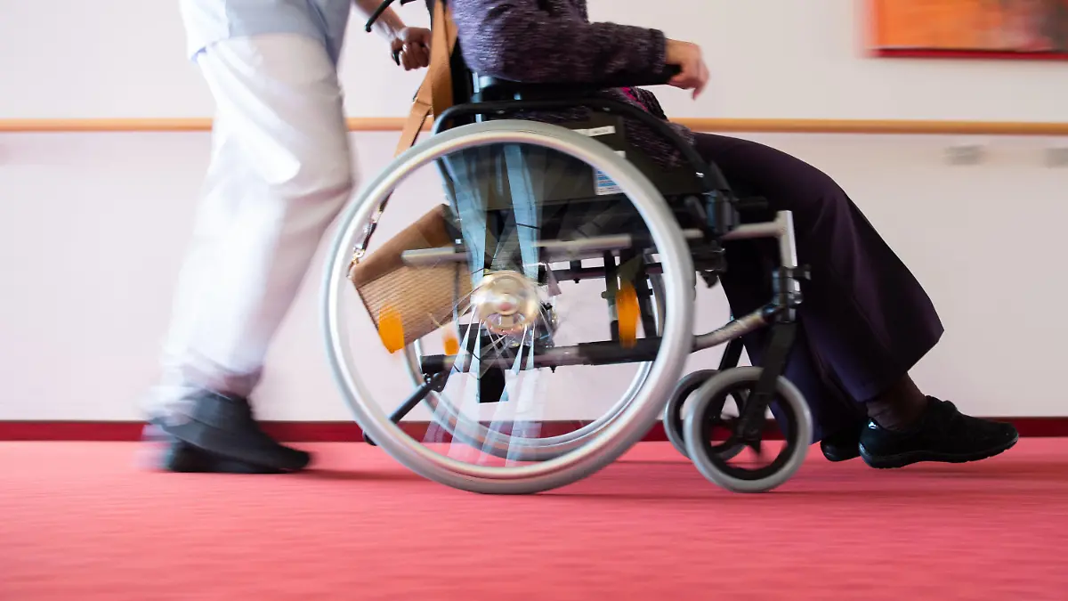 ARCHIV - 15.01.2020, Baden-Württemberg, Böblingen: Ein Pfleger schiebt eine Bewohnerin eines Pflegeheims in einem Rollstuhl über den Flur. Zum internationalen Tag der Pflege am 12. Mai demonstrieren Pflegende mit vielfältigen Aktionen für bessere Arbeitsbedingungen. (zu dpa «Pfleger protestieren im Südwesten für bessere Arbeitsbedingungen») Foto: Tom Weller/dpa +++ dpa-Bildfunk +++