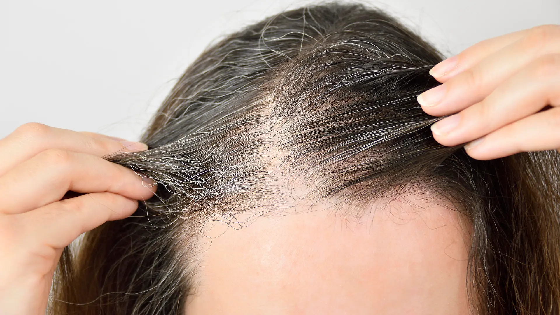 Eine Frau checkt ihre immer grauer werdenden Haare am Ansatz.