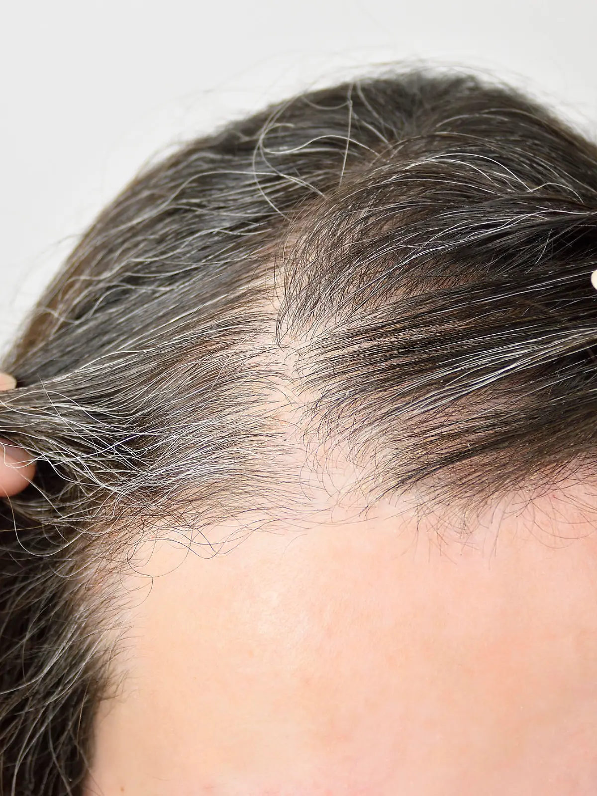 Eine Frau checkt ihre immer grauer werdenden Haare am Ansatz.