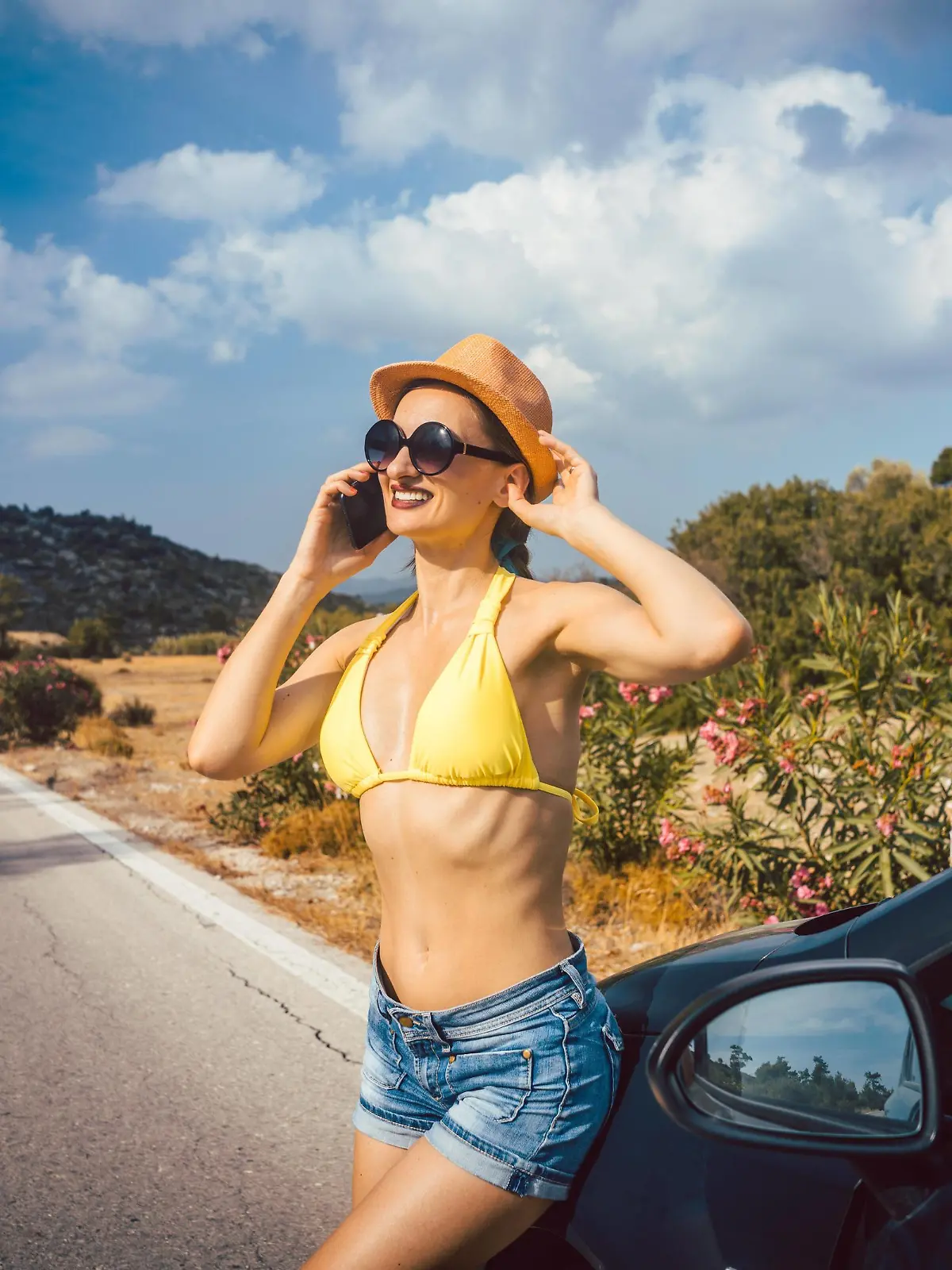 Eine Frau lehnt an ihrem Mietwagen im Hintergrund ist die Urlaubsaussicht.