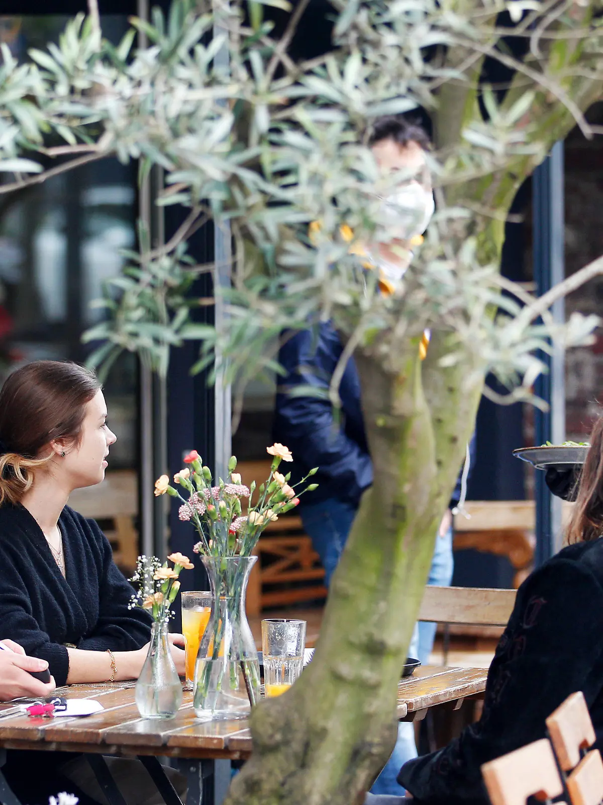 15.05.2021, Nordrhein-Westfalen, Mülheim an der Ruhr: Die Mülheimer Alina (r) und Mats unterhalten sich im Außenbereich eines Cafés in der Innenstadt mit der Kellnerin. Mülheim gehört zu den Städten in Nordrhein-Westfalen, die die Außengastronomie unter bestimmten Auflagen wieder erlauben. Foto: Roland Weihrauch/dpa +++ dpa-Bildfunk +++