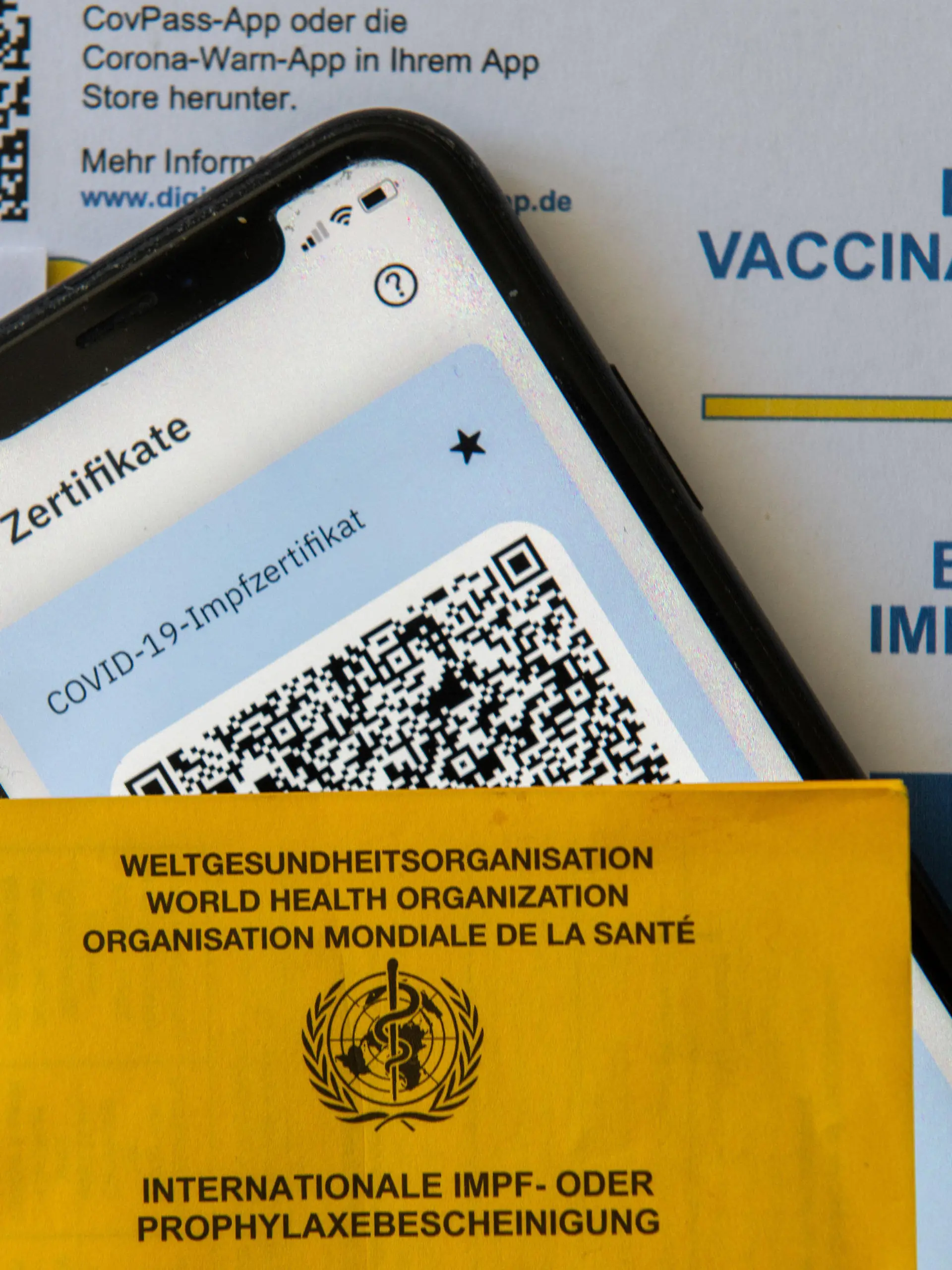 14.06.2021, Bayern, Augsburg: Ein Impfpass und ein Smartphone, auf dem die App CovPass läuft, liegen auf einem Impfzertifikat, das von einer Apotheke ausgestellt wurde. Der digitale Nachweis ist eine freiwillige Ergänzung des weiter gültigen gelben Impfheftes aus Papier. Deutschland setzt damit ein Vorhaben der Europäischen Union um. Foto: Stefan Puchner/dpa +++ dpa-Bildfunk +++
