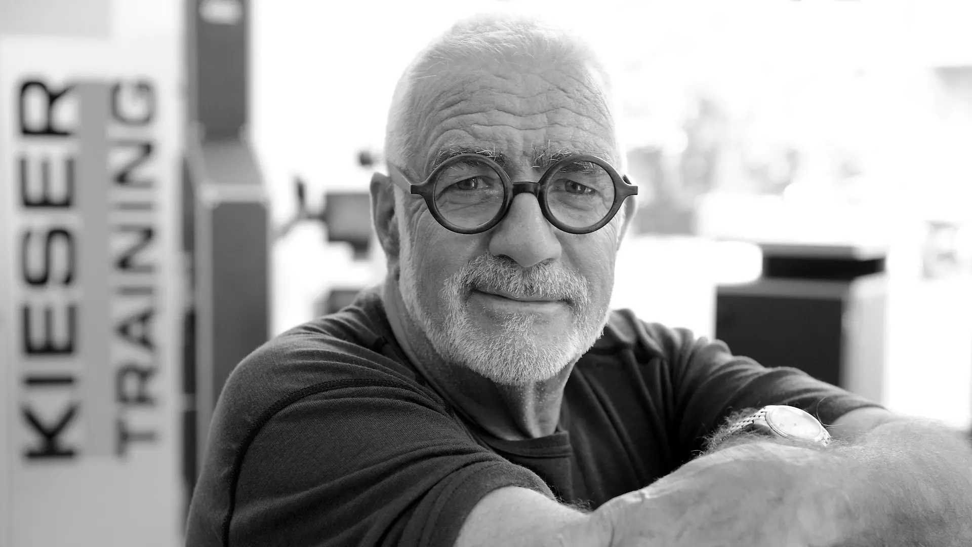 HANDOUT - 20.05.2021, ---: Werner Kieser steht vor einem Logo eines Kieser Training-Studios. Der Fitnesspionier Werner Kieser ist in Zürich im Alter von 80 Jahren an Herzversagen gestorben. (zu dpa ««Die Alten werden zu Tode geschont» - Fitnesspionier Kieser gestorben») Foto: -/Kieser Training AG/dpa - ACHTUNG: Nur zur redaktionellen Verwendung im Zusammenhang mit der aktuellen Berichterstattung und nur mit vollständiger Nennung des vorstehenden Credits +++ dpa-Bildfunk +++