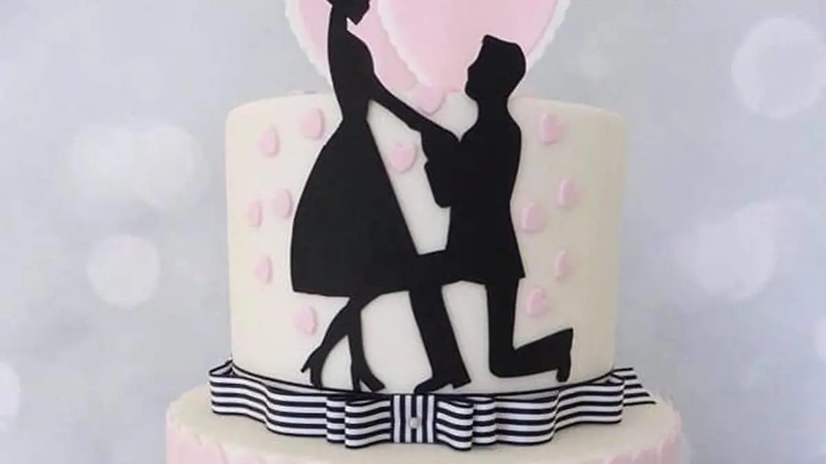 Eine mehrstöckige Torte in weiß, mit einem Miniatur-Brautpaar oben auf dem Kuchen, die für besondere Anlässe wie Verlobungen oder Hochzeiten angeboten wird.