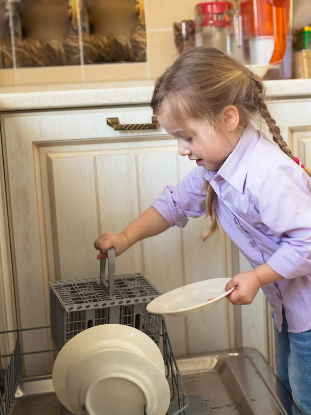 Smiling caucasian girl helping in  kitchen taking plates out of dish washing machine, casual lifestyle photo series in real life interior