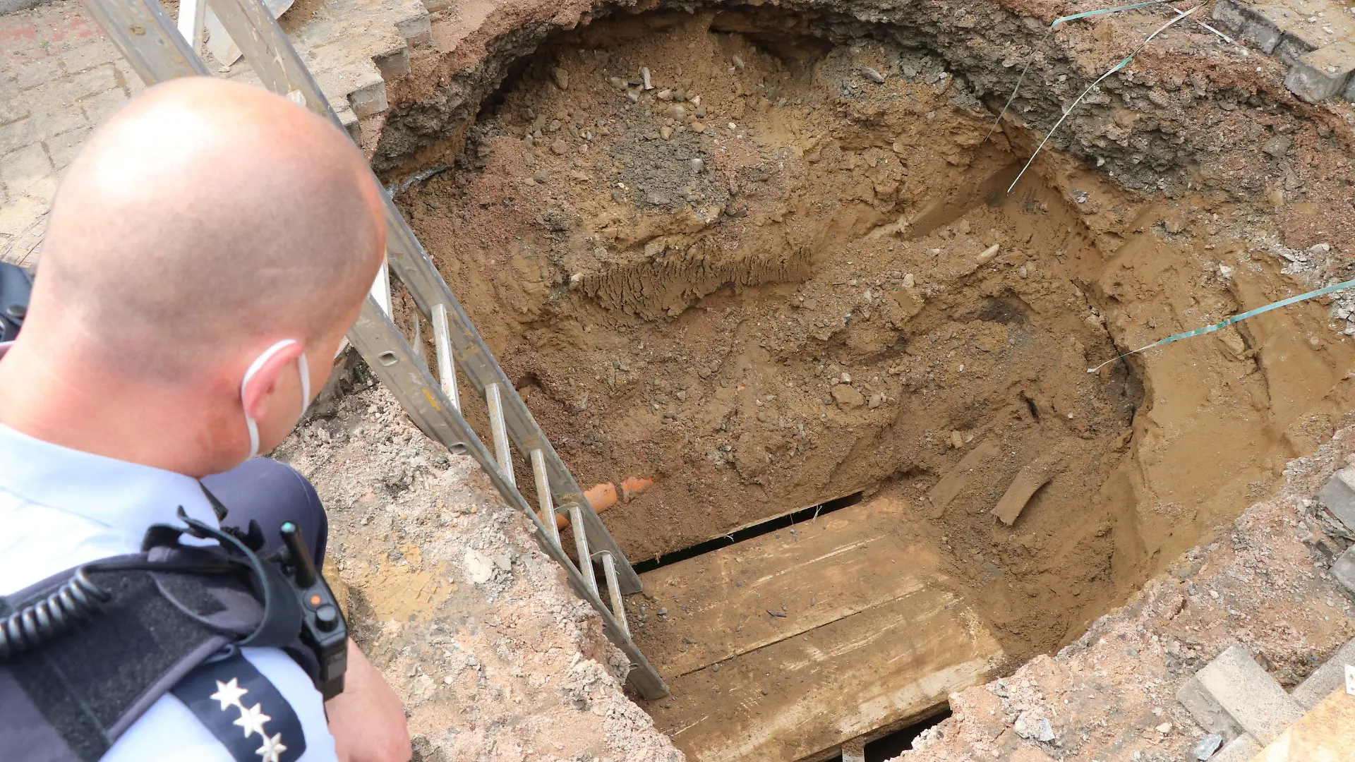 18.05.2021, Nordrhein-Westfalen, Spenge: Ein Polizist schaut auf das Loch eines Tunnels, den Unbekannte zur Volksbank gegraben haben. Einbrecher haben einen unterirdischen Tunnel bis zu einer Volksbank in Spenge (Kreis Herford) gegraben. Bauarbeiter seien darauf gestoßen, nachdem sie abgesackte Pflastersteine wieder ebnen wollten, sagte eine Polizeisprecherin am Dienstagabend. (zu dpa "Bauarbeiter entdecken Einbrecher-Tunnel zu einer Bank") Foto: Ekkehard Wind/dpa +++ dpa-Bildfunk +++