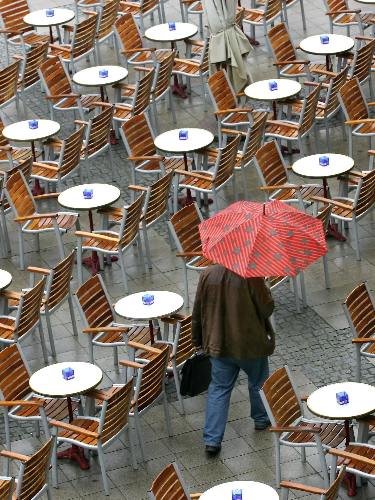 Ein Passant geht in Magdeburg mit Regenschirm durch einen leeren Biergarten (Foto vom 07.05.2007). Nach der wochenlangen Trockenheit sorgt regnerisches Wetter für Abkühlung und natürliche Bewässerung. Foto: Jens Wolf dpa/lah +++(c) dpa - Bildfunk+++