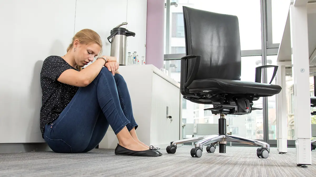 Eine Frau sitzt verzweifelt im Büro auf dem Boden.