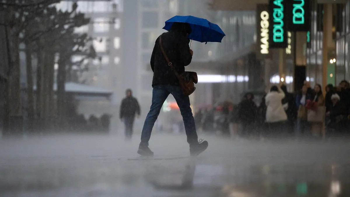 13.03.2023, Hessen, Frankfurt/Main: Ein Mann geht während eines starken Regengusses auf der Frankfurter Einkaufsstraße Zeil über die Straße. Am Rand stehen Menschen im Schutz der Vordächer der Geschäfte. Zum Wochenstart kommt es in Hessen zu teilweise starken Regenschauern. Foto: Sebastian Gollnow/dpa +++ dpa-Bildfunk +++