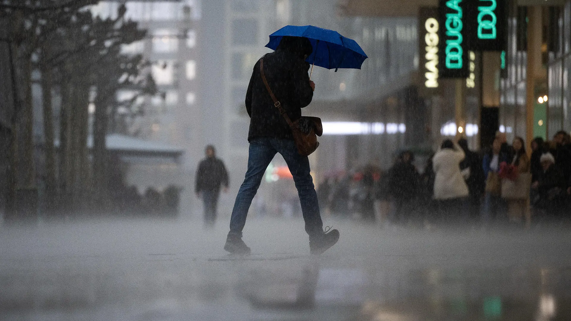 13.03.2023, Hessen, Frankfurt/Main: Ein Mann geht während eines starken Regengusses auf der Frankfurter Einkaufsstraße Zeil über die Straße. Am Rand stehen Menschen im Schutz der Vordächer der Geschäfte. Zum Wochenstart kommt es in Hessen zu teilweise starken Regenschauern. Foto: Sebastian Gollnow/dpa +++ dpa-Bildfunk +++