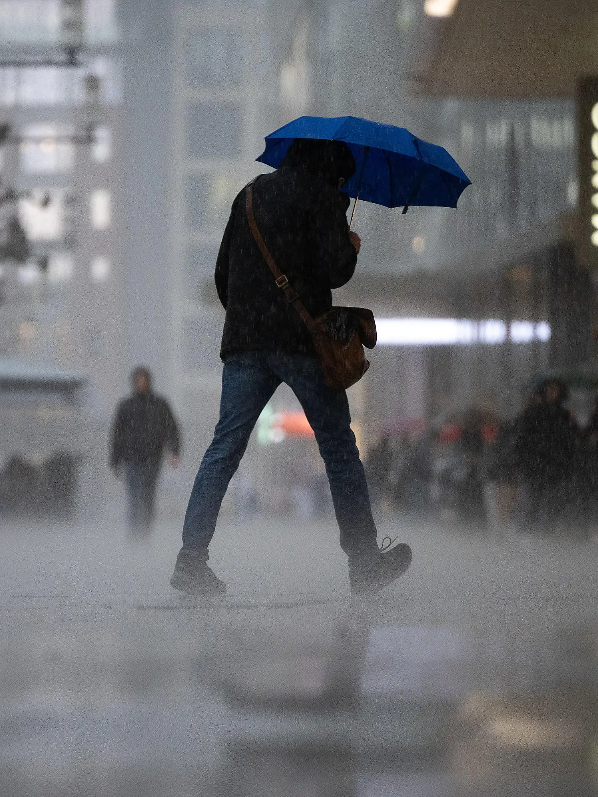 13.03.2023, Hessen, Frankfurt/Main: Ein Mann geht während eines starken Regengusses auf der Frankfurter Einkaufsstraße Zeil über die Straße. Am Rand stehen Menschen im Schutz der Vordächer der Geschäfte. Zum Wochenstart kommt es in Hessen zu teilweise starken Regenschauern. Foto: Sebastian Gollnow/dpa +++ dpa-Bildfunk +++