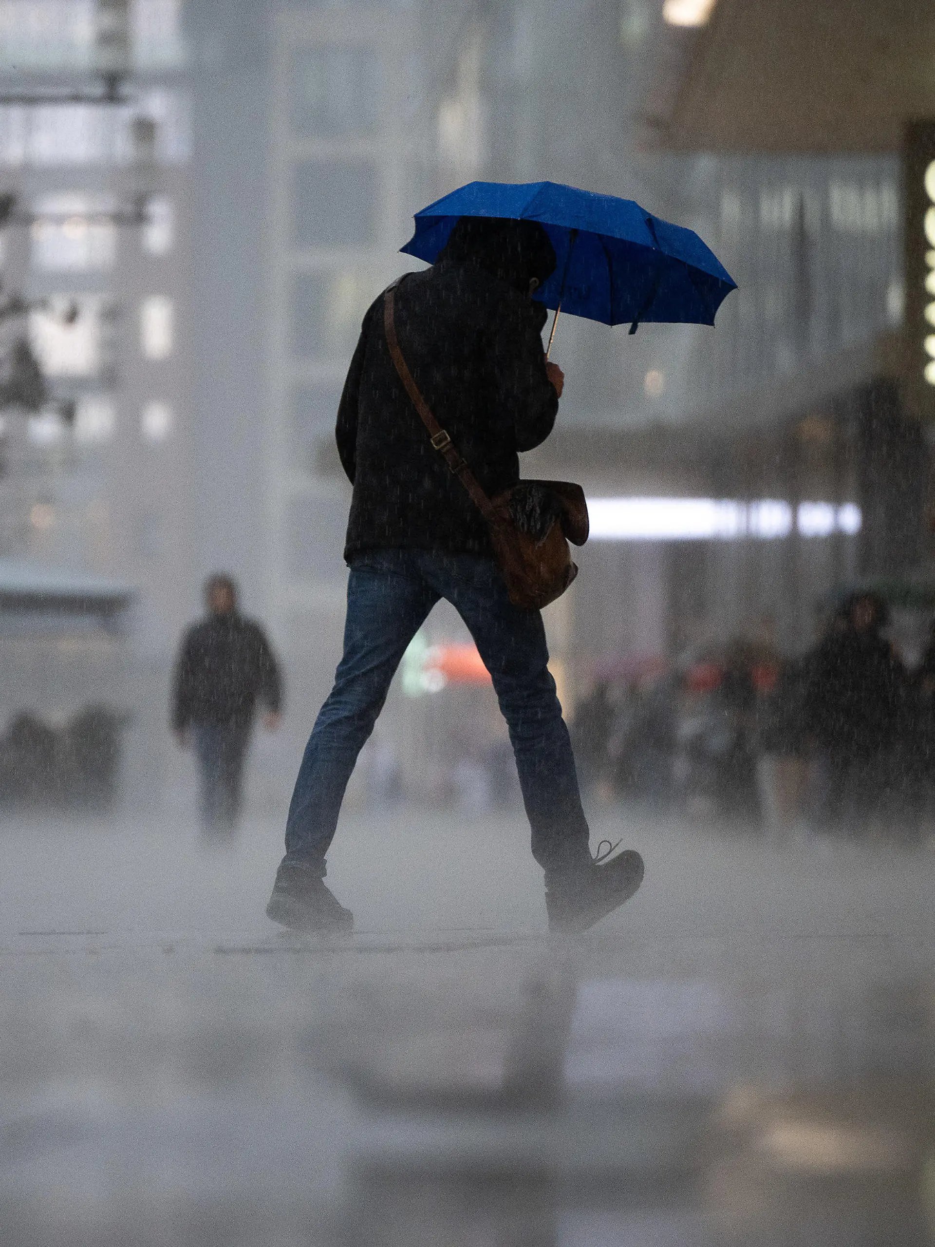 13.03.2023, Hessen, Frankfurt/Main: Ein Mann geht während eines starken Regengusses auf der Frankfurter Einkaufsstraße Zeil über die Straße. Am Rand stehen Menschen im Schutz der Vordächer der Geschäfte. Zum Wochenstart kommt es in Hessen zu teilweise starken Regenschauern. Foto: Sebastian Gollnow/dpa +++ dpa-Bildfunk +++