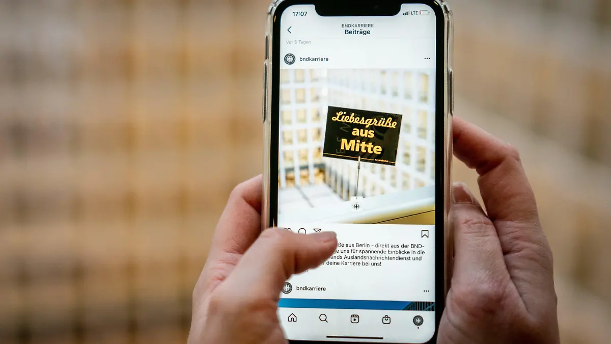 SYMBOLBILD - 12.05.2021, Berlin: Eine Mitarbeiterin zeigt in der Zentrale des Bundesnachrichtendienstes (BND), ein Foto mit einer Postkarte mit der Aufschrift ·Liebesgrüße aus Mitte·. Das Foto wird einer der ersten Instagram-Posts des deutschen Auslandsgeheimdienstes. Unter ·bndkarriere· sind auf dem Socialmedia-Kanal Instagram künftig Informationen zu Bewerbungsmöglichkeiten bei dem Geheimdienst zu finden. Foto: Kay Nietfeld/dpa +++ dpa-Bildfunk +++