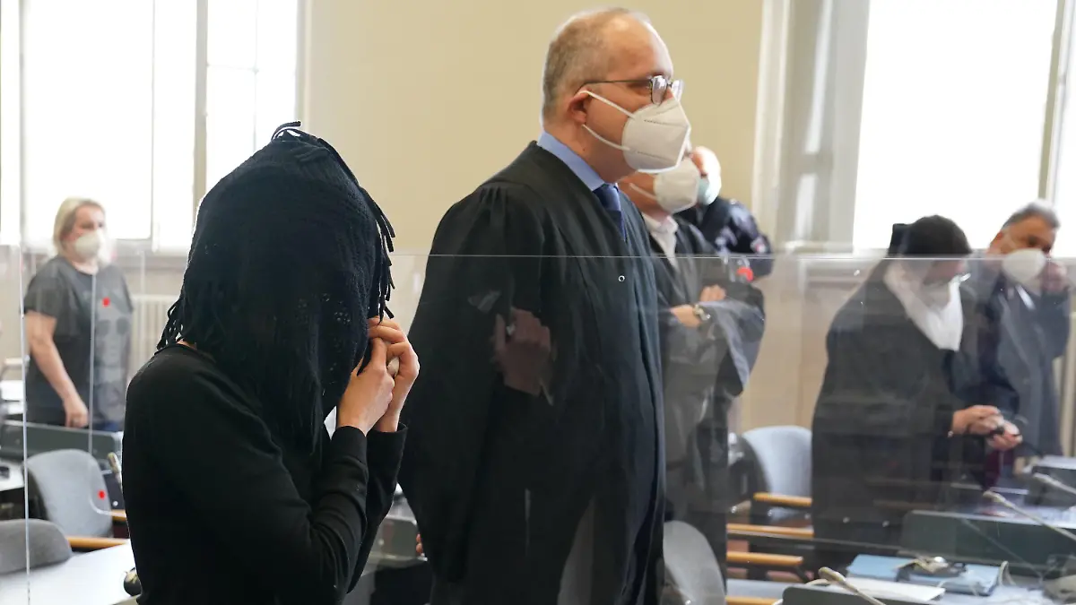 17.05.2021, Hamburg: Die Angeklagte (l) steht zu Beginn des Prozesses im Sitzungssaal, hinten rechts ist der Mitangeklagte "Milliarden-Mike" zu sehen. Die 45-jährige Polizeibeamtin soll in zehn Fällen zwischen Februar 2018 und April 2019 Daten aus polizeilichen Auskunftssystemen abgefragt und an den Angeklagten "Milliarden-Mike" weitergegeben haben. Als Gegenleistung soll sie von dem 65-Jährigen mindestens 500 Euro bekommen haben. Foto: Marcus Brandt/dpa Pool/dpa +++ dpa-Bildfunk +++