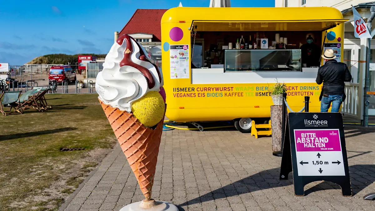 23.04.2021, Schleswig-Holstein, Wenningstedt: Ein Mann steht auf der Strandpromenade vor Imbisswagen, in dem Eis und Snacks verkauft werden. Die Gemeinde Sylt stimmt für eine Modellregion-Teilnahme. In vier Modellregionen in Schleswig-Holstein sollen die Tourismusbetriebe eine schrittweise Lockerung der Corona-Schutzmaßnahmen erproben. Foto: Axel Heimken/dpa +++ dpa-Bildfunk +++