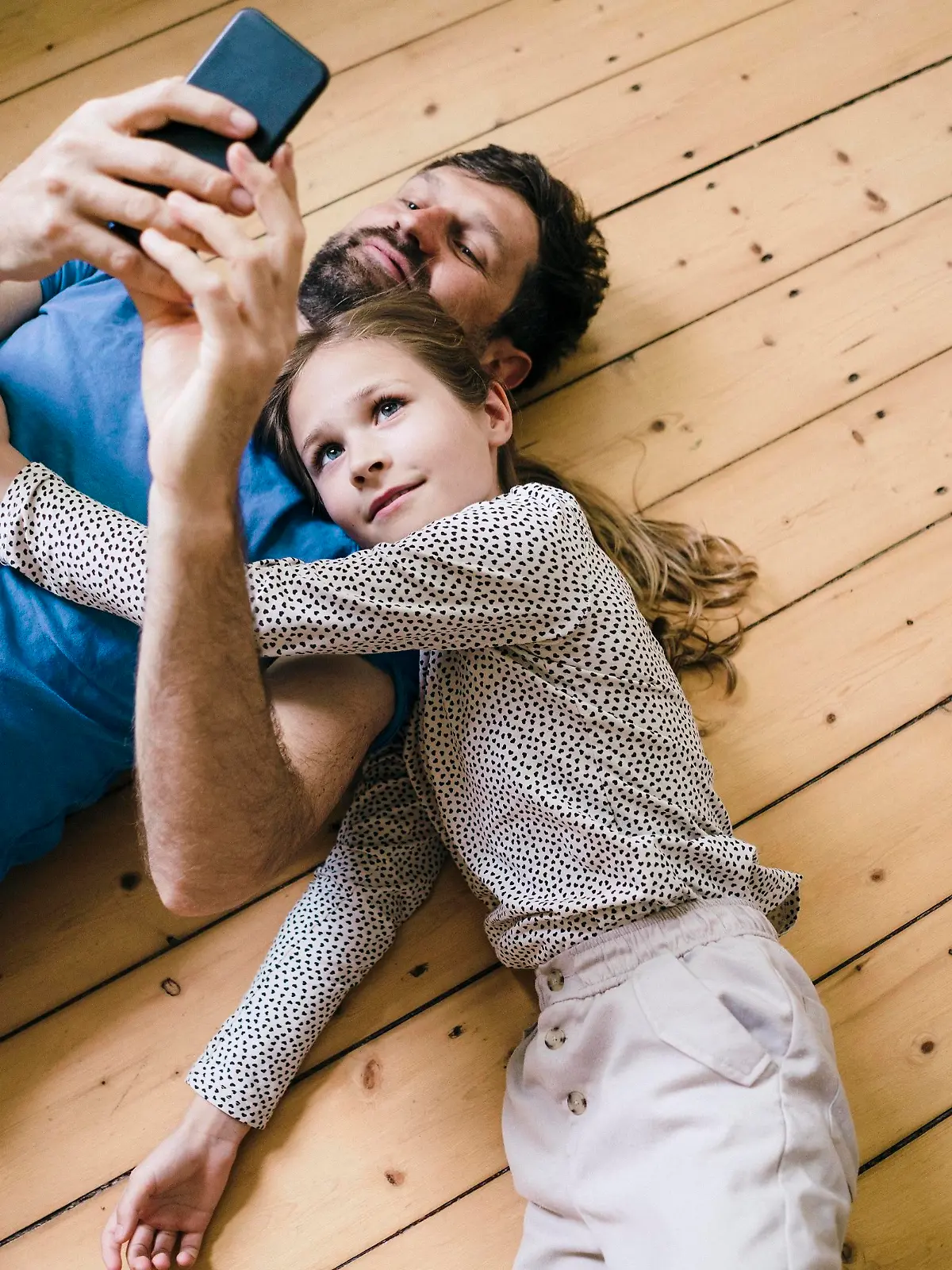 Daughter lying by father using smart phone at home || Modellfreigabe vorhanden