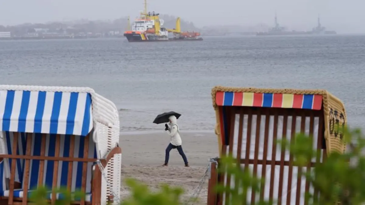 Eine Frau geht im Regen an Strand entlang