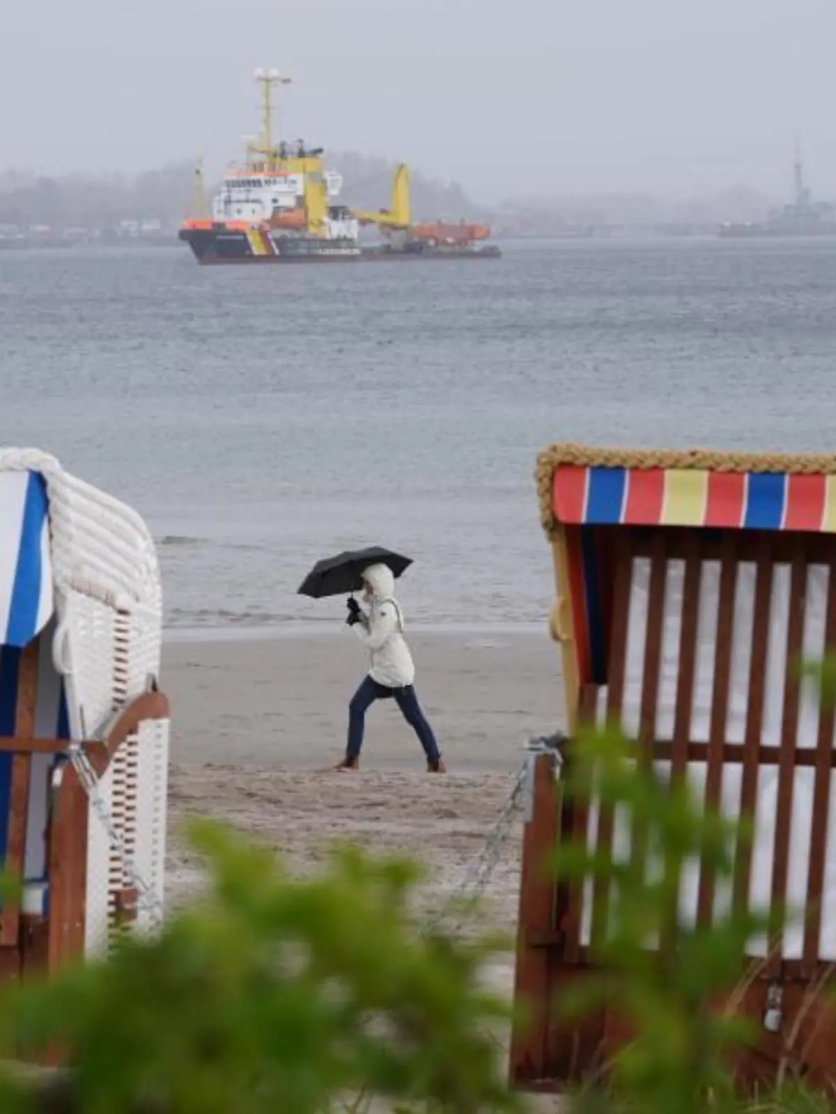 Eine Frau geht im Regen an Strand entlang