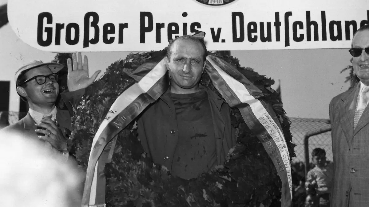 Formel 1-Fahrer Juan Manuel Fangio aus Argentinien (M) winkt am 04.08.1957 als Sieger auf Maserati beim Grossen Preis von Deutschland auf dem Nürburgring in die Kameras der Fotografen.