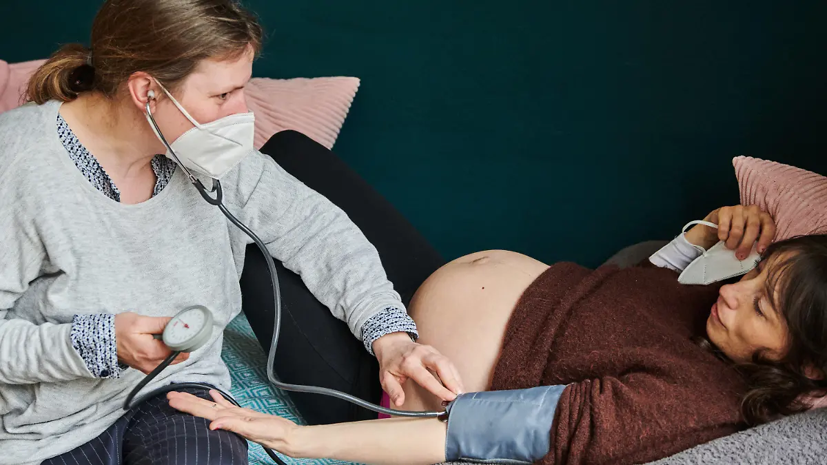 PRODUKTION - 17.04.2021, Berlin: Hebamme Grusche Nothdurft (l) misst bei Sylvia, die in der 34. Woche schwanger ist und auf einem Bett in der Praxis im Graefekiez liegt, den Blutdruck. Am 5.5.2021 ist der Internationale Hebammentag, der auf die Wichtigkeit des Berufes aufmerksam machen soll. Foto: Annette Riedl/dpa - ACHTUNG: Nur zur redaktionellen Verwendung im Zusammenhang mit einer Berichterstattung über den Internationalen Hebammentag 2021 und nur mit vollständiger Nennung des vorstehenden Credits +++ dpa-Bildfunk +++