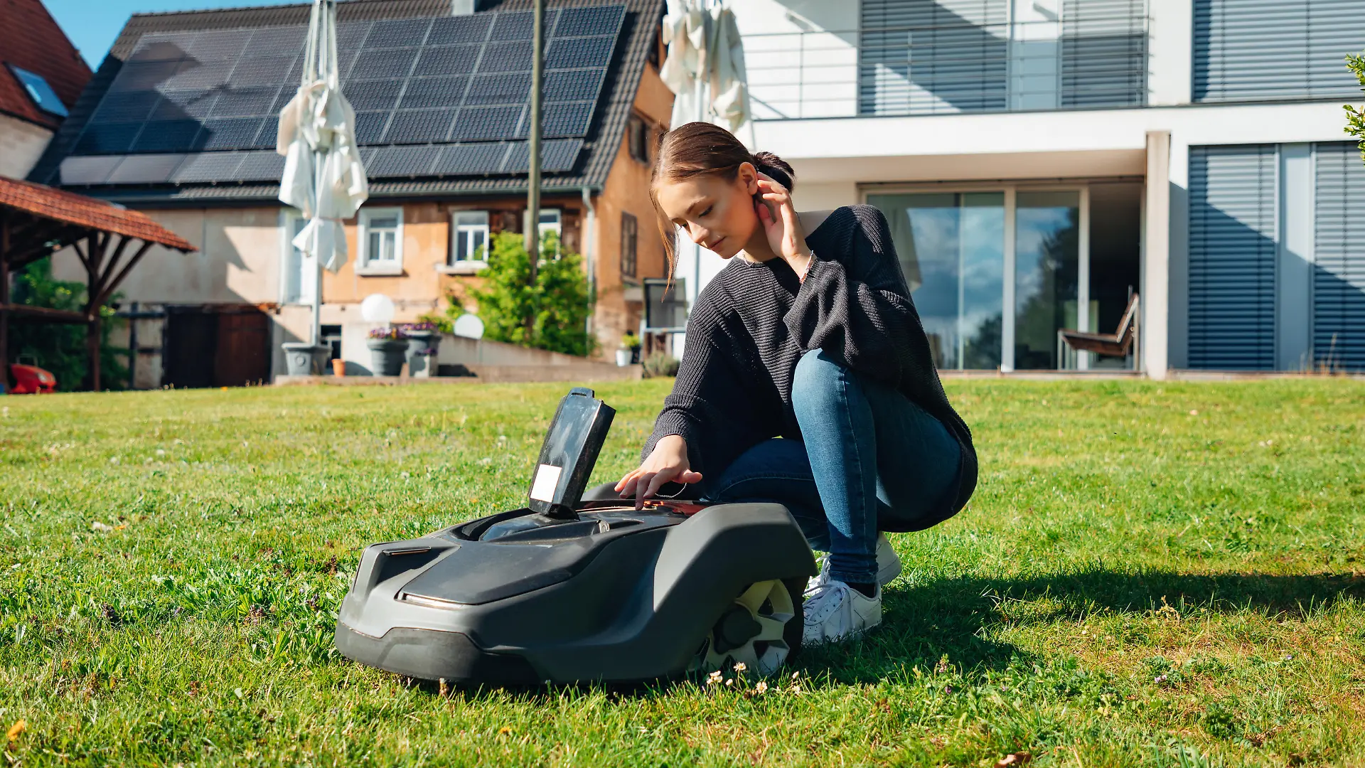 Reutlingen, Germany - April 29th, 2020: Young teenage woman programming and configuring  generic Automatic Robotic Lawn Mower in Home Garden in front of modern Home. Garden Home Automation Series - Robotic Mower Programming and Configuration