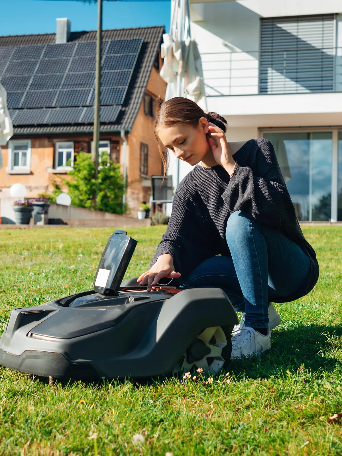 Reutlingen, Germany - April 29th, 2020: Young teenage woman programming and configuring  generic Automatic Robotic Lawn Mower in Home Garden in front of modern Home. Garden Home Automation Series - Robotic Mower Programming and Configuration