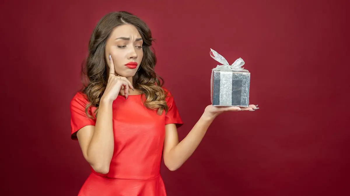 Annoyed brunette woman looking dismissively at a gift in red dress on a red background.