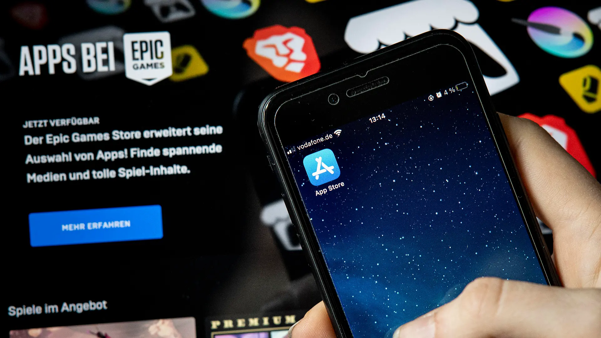 ILLUSTRATION - 02.05.2021, Berlin: Eine Frau hält ein IPhone mit dem Appstore vor einem Bildschirm, auf dem der Epic Games Store zu sehen ist. Epic, Macher des populären Spiels "Fortnite", will digitale Artikel in seinen Apps verkaufen, ohne einen Anteil vom Kaufpreis an Apple abzugeben. Der Konflikt könnte verändern, wie das Geschäft mit Apps und digitalen Inhalten läuft. Foto: Fabian Sommer/dpa +++ dpa-Bildfunk +++