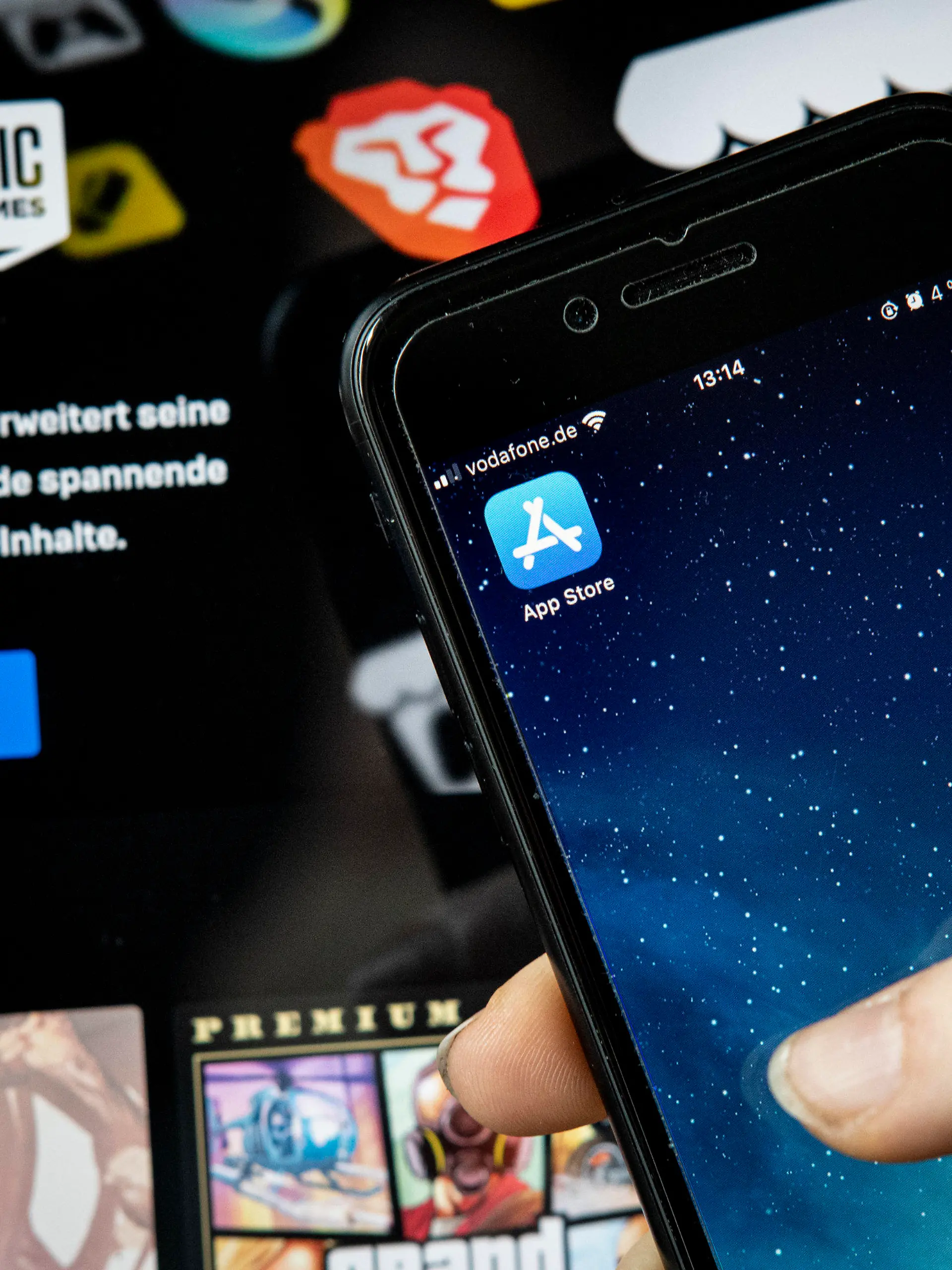 ILLUSTRATION - 02.05.2021, Berlin: Eine Frau hält ein IPhone mit dem Appstore vor einem Bildschirm, auf dem der Epic Games Store zu sehen ist. Epic, Macher des populären Spiels "Fortnite", will digitale Artikel in seinen Apps verkaufen, ohne einen Anteil vom Kaufpreis an Apple abzugeben. Der Konflikt könnte verändern, wie das Geschäft mit Apps und digitalen Inhalten läuft. Foto: Fabian Sommer/dpa +++ dpa-Bildfunk +++