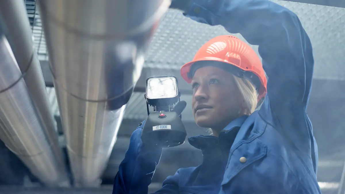 Technikerin, Monteurin mit orangen Helm und Lampe kontrolliert Rohrleitungen,