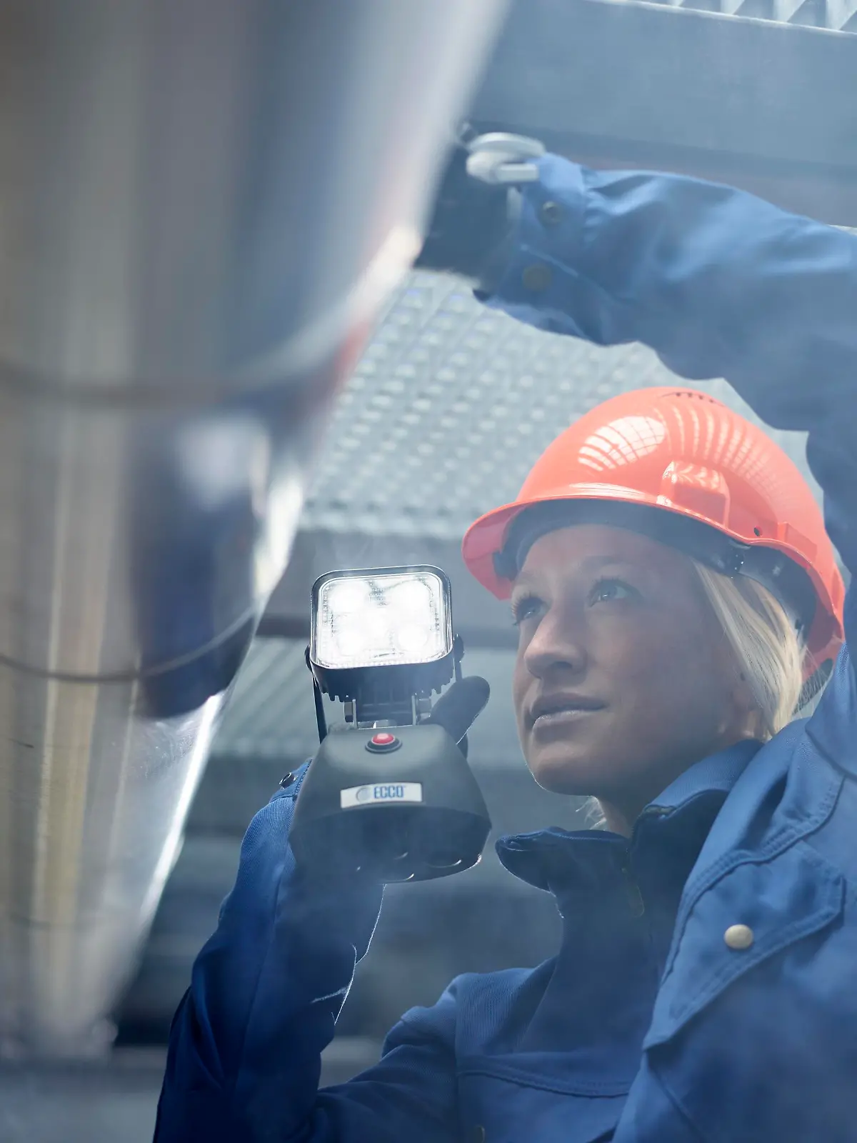 Technikerin, Monteurin mit orangen Helm und Lampe kontrolliert Rohrleitungen,