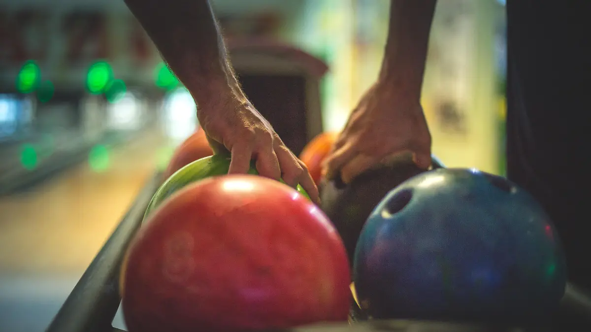 Hände greifen zur Bowlingkugel an der Bowlingbahn